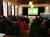 In der Aula folgt das Publikum Dominik Birkholz aus der Klasse SGA 21 bei seinem Vortrag zur Verteidigung seiner Projektarbeit. Im Hintergrund ist eine Leinwand mit der Präsentation zu sehen.